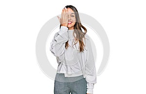 Young brunette woman wearing casual turtleneck sweater covering one eye with hand, confident smile on face and surprise emotion