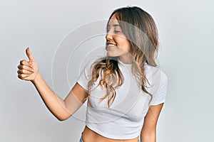 Young brunette woman wearing casual white t shirt looking proud, smiling doing thumbs up gesture to the side