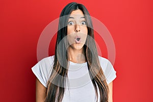 Young brunette woman wearing casual white tshirt over red background afraid and shocked with surprise expression, fear and excited