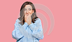 Young brunette woman wearing casual winter sweater laughing and embarrassed giggle covering mouth with hands, gossip and scandal