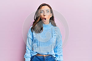 Young brunette woman wearing casual winter sweater over pink background afraid and shocked with surprise expression, fear and