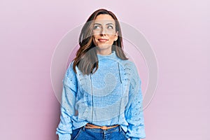 Young brunette woman wearing casual winter sweater over pink background smiling looking to the side and staring away thinking