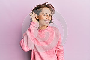 Young brunette woman wearing casual winter sweater smiling with hand over ear listening and hearing to rumor or gossip