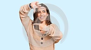 Young brunette woman wearing casual winter sweater smiling making frame with hands and fingers with happy face