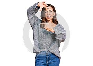 Young brunette woman wearing casual winter sweater smiling making frame with hands and fingers with happy face