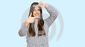 Young brunette woman wearing casual winter sweater smiling making frame with hands and fingers with happy face