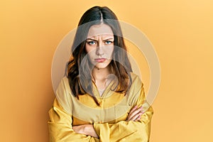 Young brunette woman wearing casual yellow shirt skeptic and nervous, disapproving expression on face with crossed arms