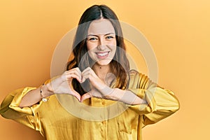 Young brunette woman wearing casual yellow shirt smiling in love showing heart symbol and shape with hands