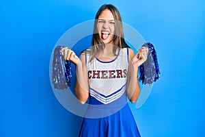 Young brunette woman wearing cheerleader uniform sticking tongue out happy with funny expression