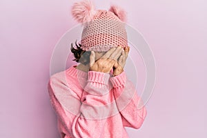 Young brunette woman wearing cute wool cap with sad expression covering face with hands while crying