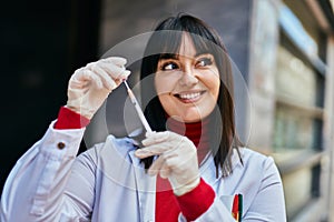 Young brunette woman wearing doctor uniform holding syringe and vaccine at the city