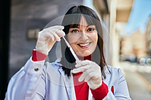 Young brunette woman wearing doctor uniform holding syringe and vaccine at the city