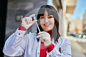 Young brunette woman wearing doctor uniform holding syringe and vaccine at the city