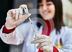 Young brunette woman wearing doctor uniform holding syringe and vaccine at the city