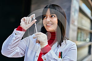 Young brunette woman wearing doctor uniform holding syringe and vaccine at the city
