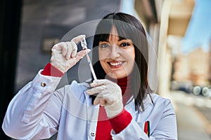 Young brunette woman wearing doctor uniform holding syringe and vaccine at the city