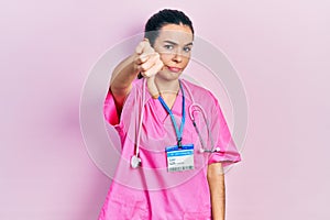 Young brunette woman wearing doctor uniform and stethoscope looking unhappy and angry showing rejection and negative with thumbs