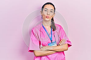 Young brunette woman wearing doctor uniform and stethoscope standing with arms crossed looking at the camera blowing a kiss being