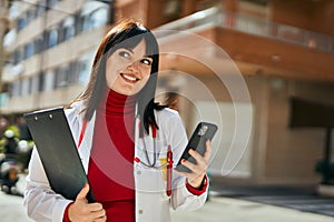 Young brunette woman wearing doctor uniform using smartphone at the city