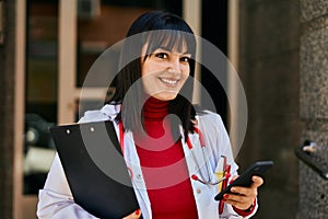 Young brunette woman wearing doctor uniform using smartphone at house entrance
