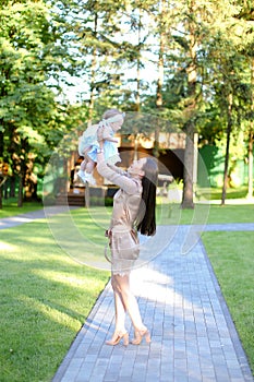 Young brunette woman wearing dress holding little baby in garden.