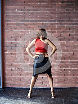 Young brunette woman, wearing red top and black leather skirt, dancing posing in spacious studio loft room with huge window.