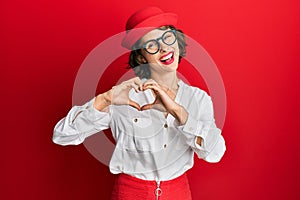 Young brunette woman wearing stewardess style and glasses smiling in love showing heart symbol and shape with hands