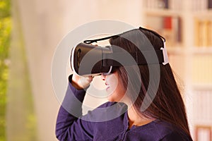 Young brunette woman wearing virtual reality goggles experiencing future technology, interacting and smiling while