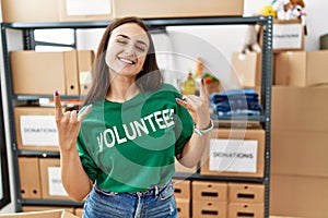 Young brunette woman wearing volunteer t shirt at donations stand shouting with crazy expression doing rock symbol with hands up