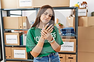 Young brunette woman wearing volunteer t shirt at donations stand suffering pain on hands and fingers, arthritis inflammation