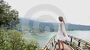 Young brunette woman in white dress spinning dancing on viewpoint with a view on Munduk Lake, Travel destination Bali