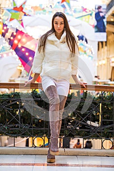 Young brunette woman in white fur coat and high suede boots