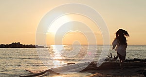 Young brunette woman in a white shirt running on the beach at sunset. Back view.