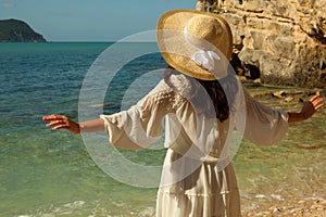 Young brunette woman in white summer dress with straw hat looking to a sea.