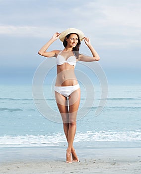 A young brunette woman in a white swimsuit on the beach