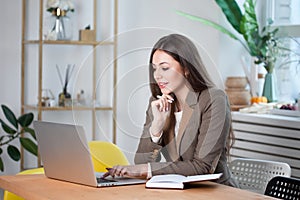 Young brunette woman working on a laptop in a bright comfortable office.