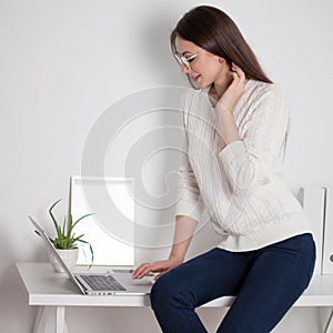 Young brunette woman working on a laptop in a bright comfortable office.