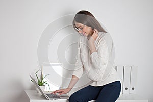 Young brunette woman working on a laptop in a bright comfortable office.