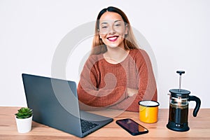 Young brunette woman working at the office drinking a cup of coffee happy face smiling with crossed arms looking at the camera