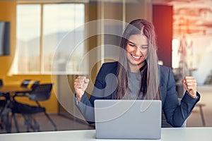 Young brunette woman working at the office with laptop success sign doing positive gesture with hand, thumbs up smiling