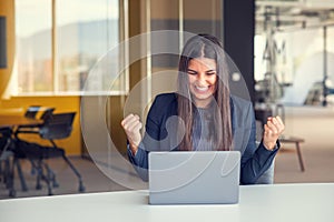 Young brunette woman working at the office with laptop success sign doing positive gesture with hand, thumbs up smiling