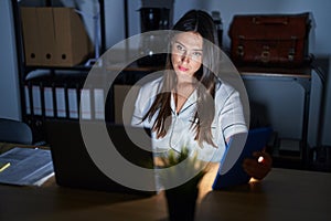 Young brunette woman working at the office at night looking sleepy and tired, exhausted for fatigue and hangover, lazy eyes in the