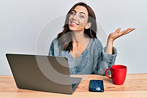 Young brunette woman working at the office using computer laptop celebrating achievement with happy smile and winner expression