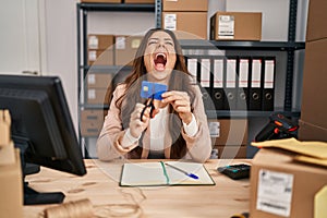 Young brunette woman working at small business ecommerce cutting credit card angry and mad screaming frustrated and furious,