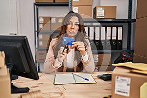 Young brunette woman working at small business ecommerce cutting credit card depressed and worry for distress, crying angry and