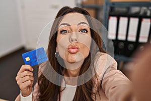 Young brunette woman working at small business ecommerce holding credit card looking at the camera blowing a kiss being lovely and