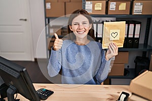 Young brunette woman working at small business ecommerce smiling happy and positive, thumb up doing excellent and approval sign