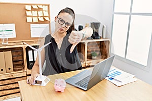 Young brunette woman working on solar windmill for cheaper electricity with angry face, negative sign showing dislike with thumbs