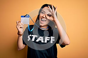 Young brunette worker woman wearing staff t-shirt as uniform showing id card with happy face smiling doing ok sign with hand on