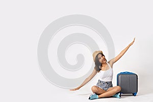 Young bruntte girl traveler with luggage case and summer hat flying like airplane in white isolated background.
